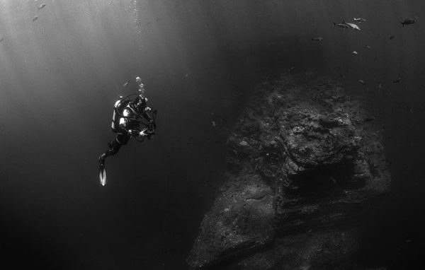 photo noir et blanc d'un plongeur au dessus d'une épave