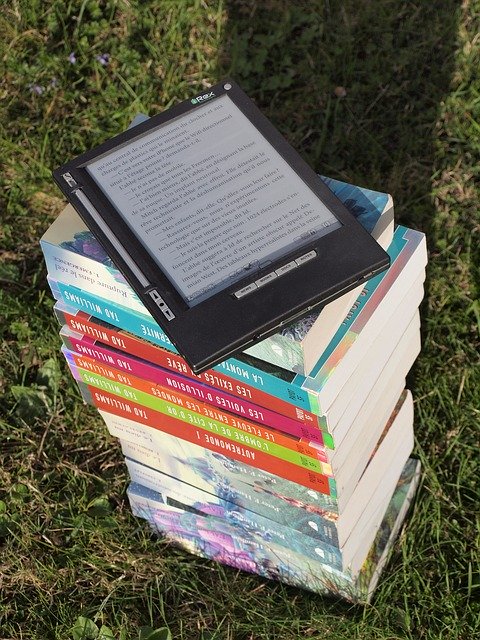 pile de livres dans l'herbe sur laquelle trône une liseuse